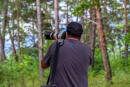 A photographer is poised among tall trees, using a large camera lens to capture wildlife in a...