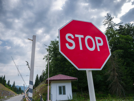 Bright red stop sign at a rural intersection with trees and clouds.