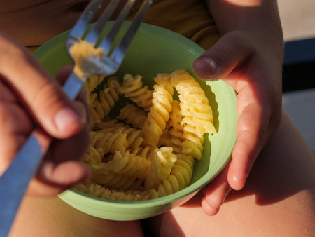 Child holds a green bowl of pasta while enjoying a warm day outside.の写真素材