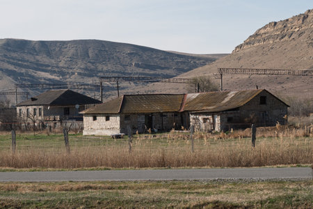 Abandoned farmhouse silhouettes punctuating barren terrain, power lines stretching toward distant mountain rangesの写真素材
