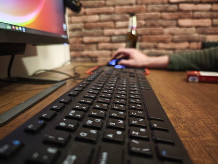 Close up of a black keyboard on a wooden desk, with a programmer using a mouse and working on a...