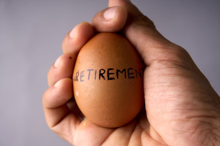 Hand holding brown egg labeled 'RETIREMENT' in black ink. Symbolizes savings, planning, and financial security.の写真素材