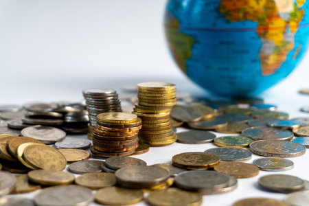 Stacks of mixed coins with a world globe in the background, symbolizing global finance, economic growth, investment, currency value, and international markets.の写真素材