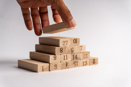 Hand placing numbered wooden block on pyramid stack, symbolizing strategy, focus, planning, learning, and building success step by step.の写真素材