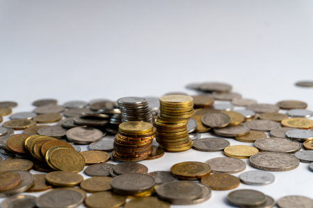 Stacks of mixed silver and gold coins scattered on a white surface, symbolizing savings, wealth, investment, financial planning, and economic concepts.の写真素材