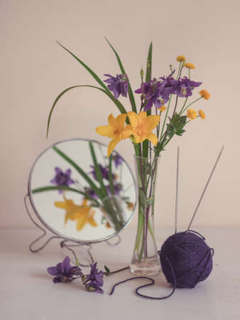 Still life with yellow and blue flowers in a glass vase and the ball of knitting yarn. Floral...
