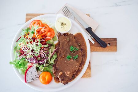 Grilled beef steak served with French fries and vegetables on a white plate.