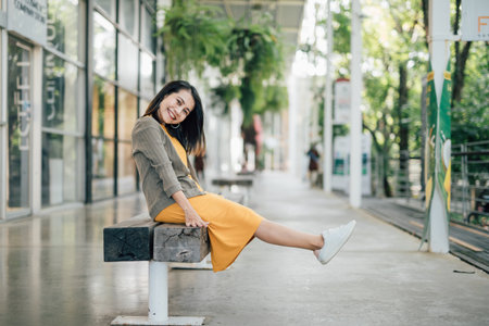 A young woman in yellow sits on another nine and raises both legs above the floor in a happy and...