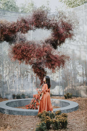 A beautiful woman dressed in a brown dress in the middle of a forest rich in colorful flowers, beautiful during daytime, touring the flower garden and taking pictures for relaxing and happy vacation.の写真素材