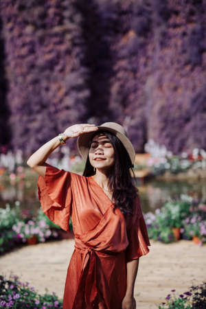 A beautiful woman dressed in a brown dress in the middle of a forest rich in colorful flowers, beautiful during daytime, touring the flower garden and taking pictures for relaxing and happy vacation.の写真素材