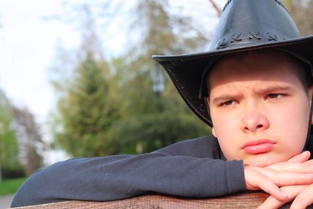 Young cowboy with black leather hat looking at the sunset. Blurred forest background.の写真素材