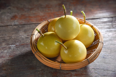 Passion fruit (Maracuya) in a bamboo tray with green leaves on a wooden table background.