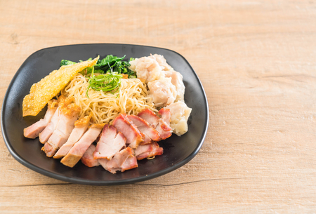Egg noodle with red roast pork, crispy pork, dumplings, soup and condimentsの写真素材