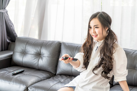 young asian woman changing tv channel at home in the living room - selective focus pointの写真素材
