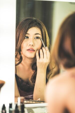 Young Beautiful Asian Woman making make-up near mirror - vintage effect filterの写真素材