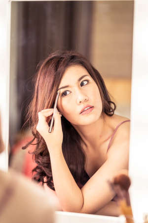 Young Beautiful Asian Woman making make-up near mirror - vintage effect filterの写真素材