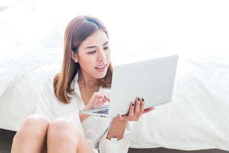 Beautiful asian woman working at home with laptop and telephoneの写真素材