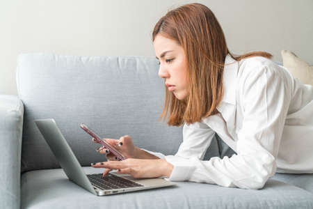 Beautiful asian woman working at home with laptop and telephoneの写真素材