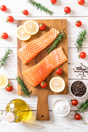 Raw salmon fillet with tomatoes lemon rosemary pepper and salt on wood boardの写真素材