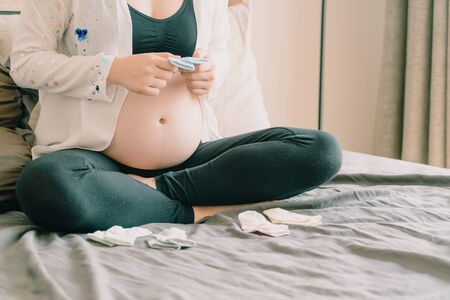 Belly of pregnant woman with hands choosing baby socks - selective focus point with vintage filter...