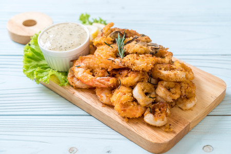 fried seafood (squids, shrimps, mussels) with sauce on wooden boardの写真素材