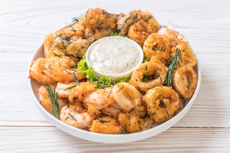 fried seafood (squids, shrimps, mussels) with sauce on wooden boardの写真素材