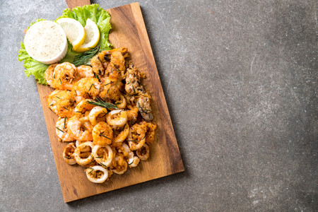 fried seafood (squids, shrimps, mussels) with sauce on wooden boardの写真素材