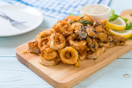 fried seafood (squids, shrimps, mussels) with sauce on wooden boardの写真素材