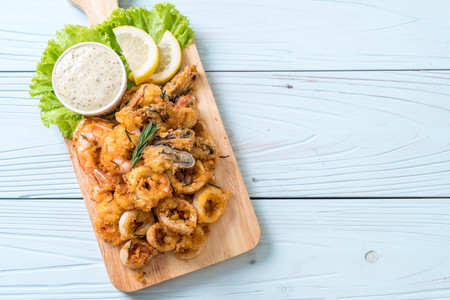 fried seafood (squids, shrimps, mussels) with sauce on wooden boardの写真素材