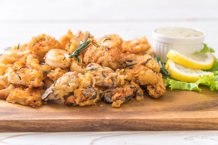 fried seafood (squids, shrimps, mussels) with sauce on wooden boardの写真素材