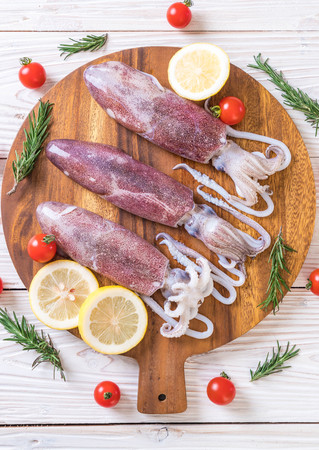 fresh octopus or squids raw on wooden board with ingredients