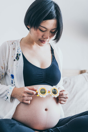Young beautiful Asian pregnant woman with flower sunglasses on her belly at home - selective focus point and vintage  styleの写真素材