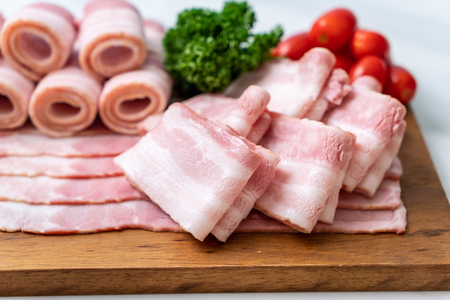 sliced raw pork bacon on wood boardの写真素材