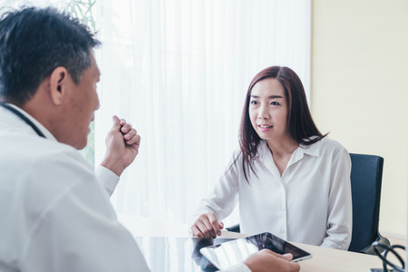 Asian female patient and doctor are discussing something while sitting at the tableの写真素材