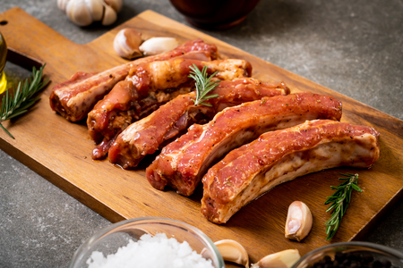 Fresh raw pork ribs ready for roasting with ingredients on wooden boardの写真素材