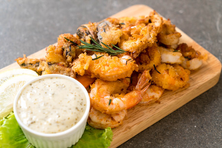 fried seafood (squids, shrimps, mussels) with sauce on wooden board
