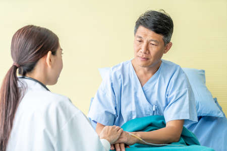 Asian female doctor reassuring on her senior patient hand - selective focus pointの写真素材