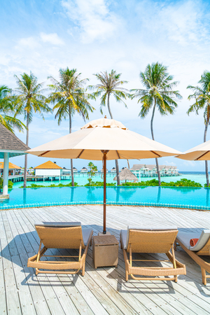 Umbrella and chair around swimming pool in resort hotel with beach and sea background in Maldivesの写真素材