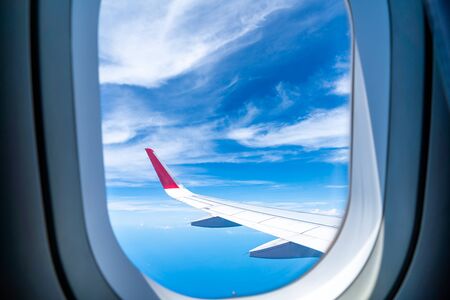 Clouds and sky as seen through window of an aircraft with airplane's wing