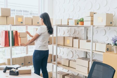Asian Women business owner working at home with packing box on workplace - online shopping SME entrepreneur or freelance working conceptの写真素材