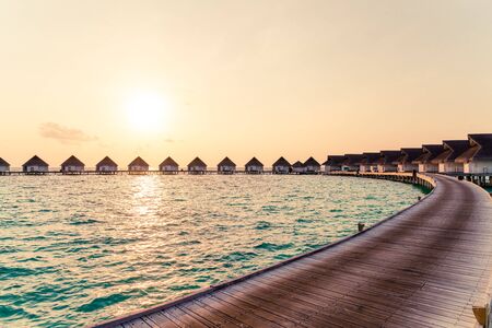 Beautiful tropical sunset over Maldives island with water bungalow in hotel resort