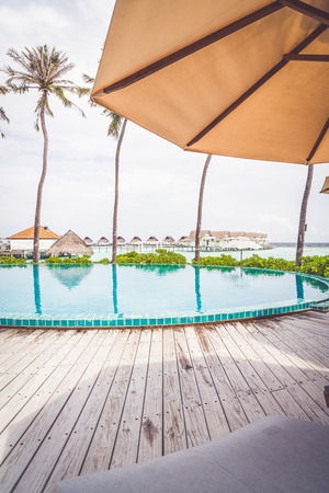 Umbrella and chair around swimming pool in resort hotel with beach and sea background in Maldivesのeditorial素材