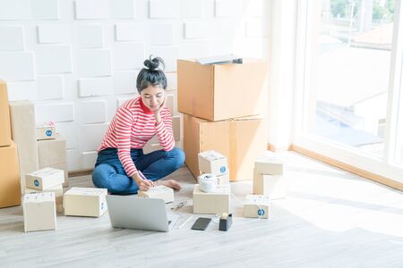 Asian Women business owner working at home with packing box on workplace - online shopping SME...