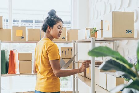 young Asian woman  checking goods on stock shelf at warehouse - online selling or shopping online conceptの写真素材