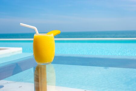mango smoothies glass with swimming pool and sea beach background