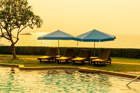 Beach chair or pool bed with umbrella around swimming pool with sunset and sea