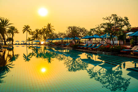 beautiful palm tree with umbrella chair pool in luxury hotel resort at sunrise times - holiday and vacation concept