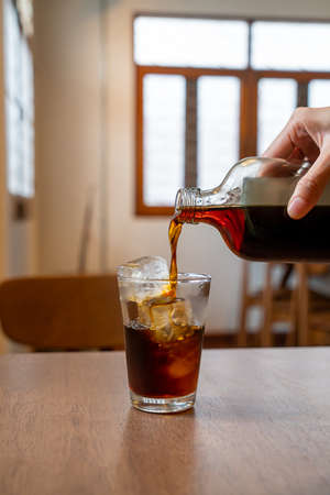 pouring cold brew coffee in glass with ice cube on wood tableの写真素材
