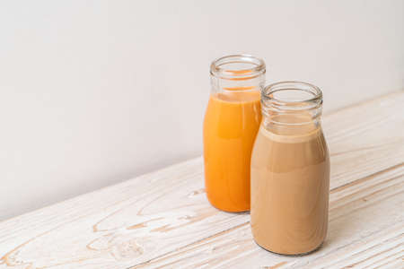 Thai milk tea and coffee with milk in bottle on wood tableの写真素材
