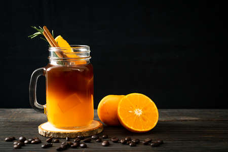 A glass of iced americano black coffee and layer of orange and lemon juice decorated with rosemary and cinnamonの写真素材